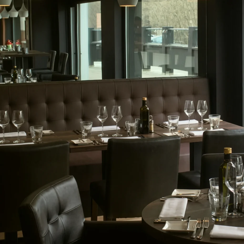 Het interieur van Brasserie Sapore met zwarte lederen banken en gedekte tafels bij het raam